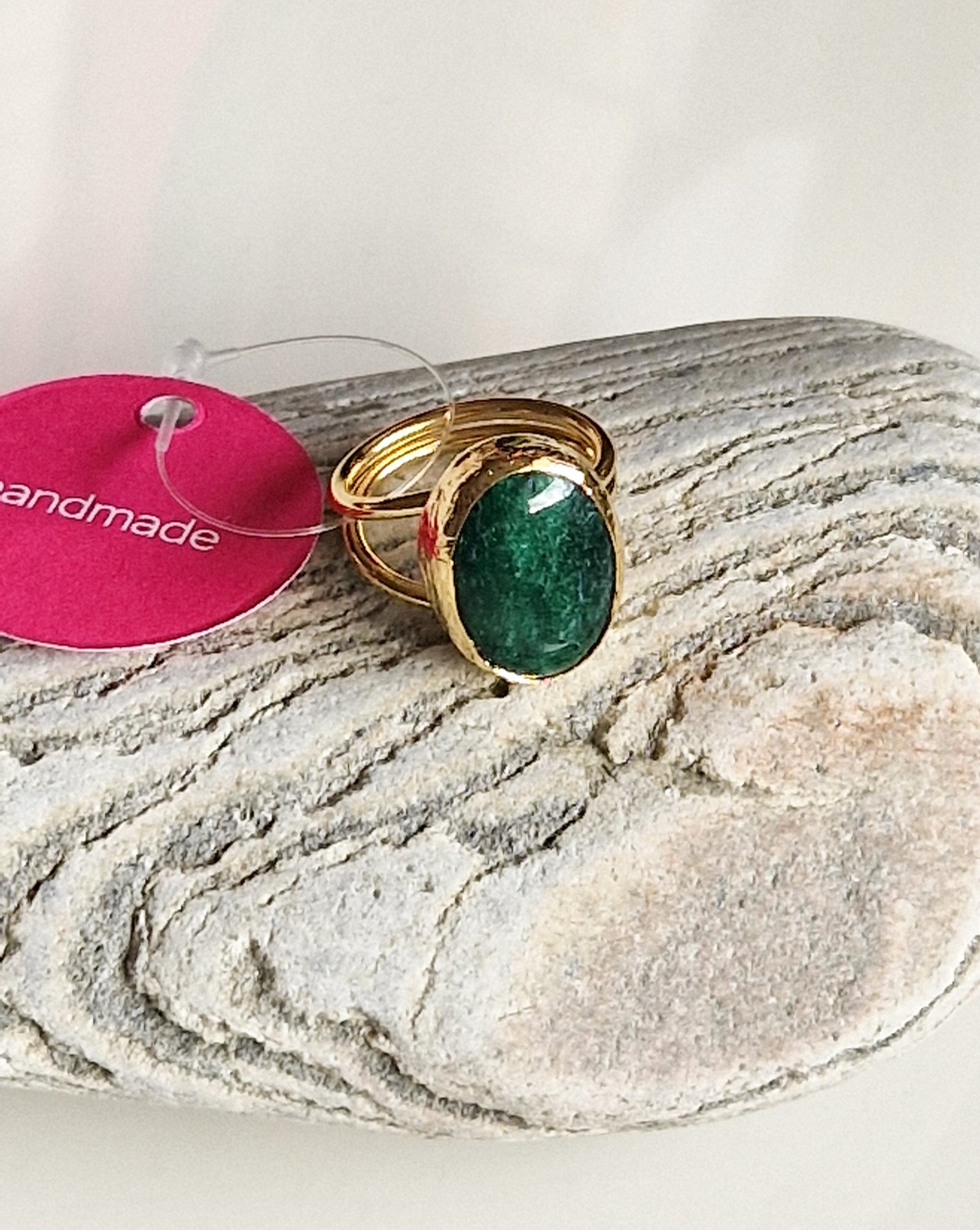 Gold ring with a green gemstone on a stone surface, with a 'handmade' tag in the background.
