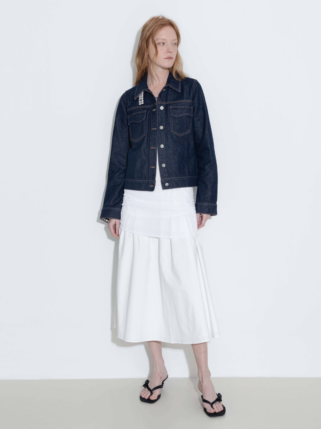 Person wearing a dark denim jacket and white skirt on a plain background