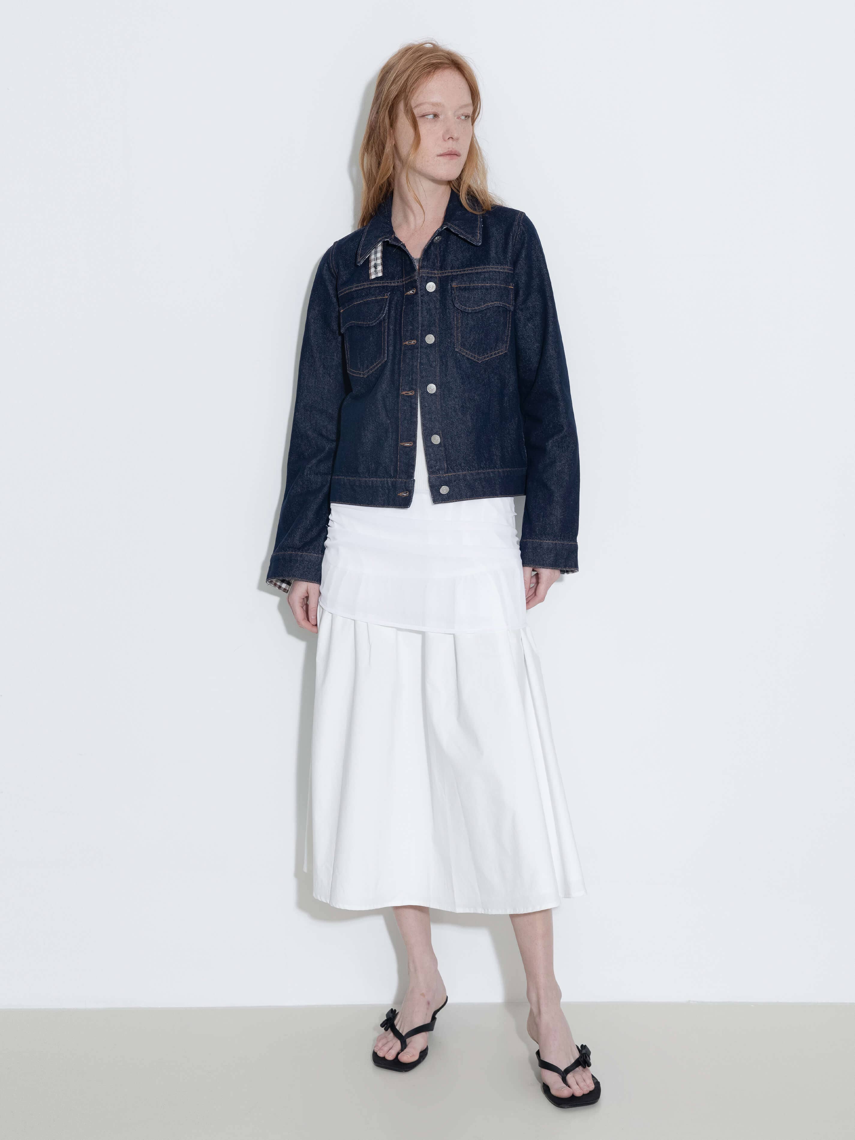 Person wearing a dark denim jacket and white skirt on a plain background