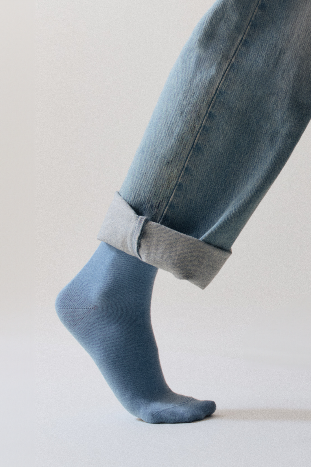 Person wearing blue jeans with rolled-up cuffs and matching blue socks on a light background
