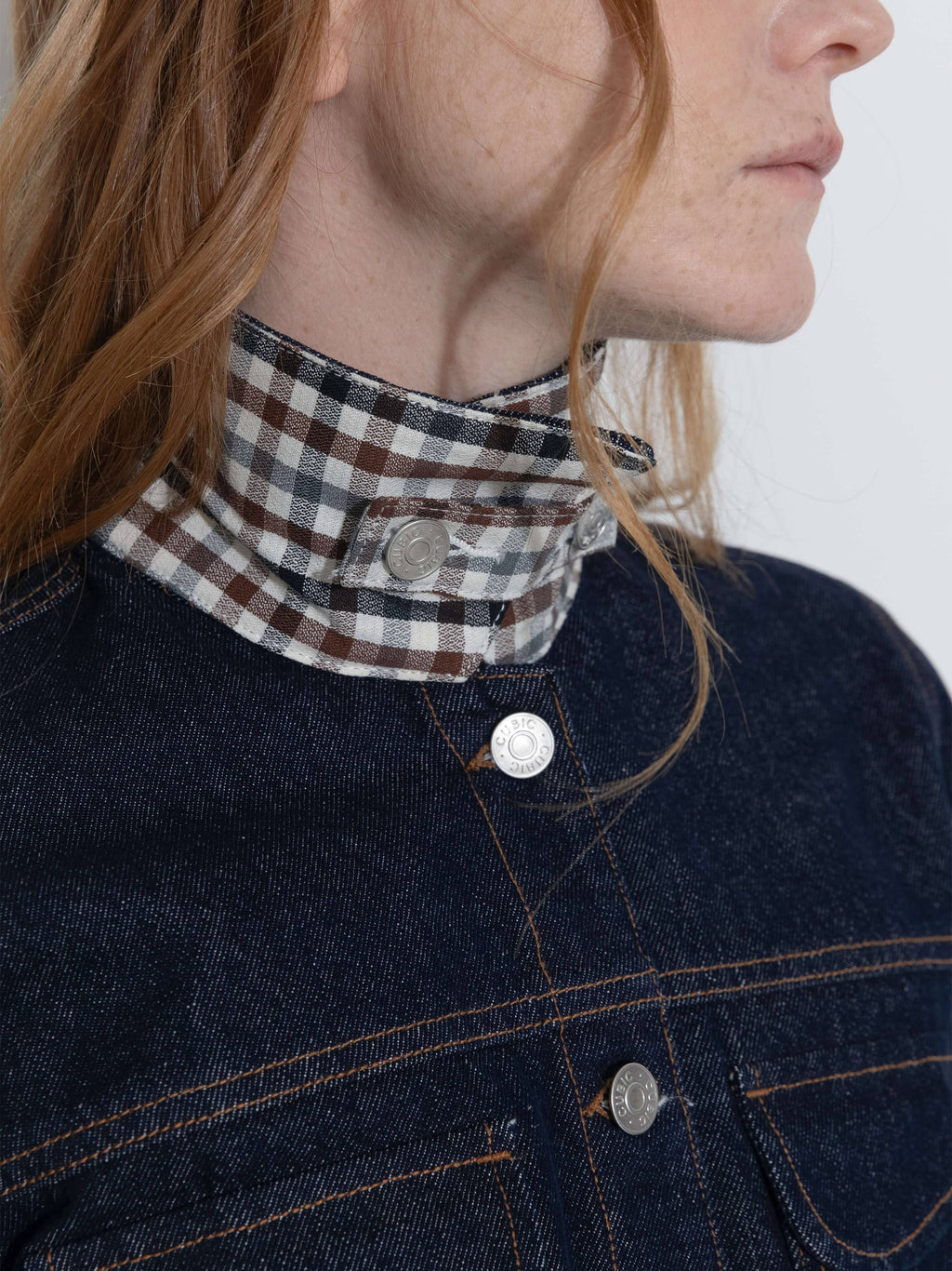 Person wearing a dark denim jacket with a plaid scarf around their neck.