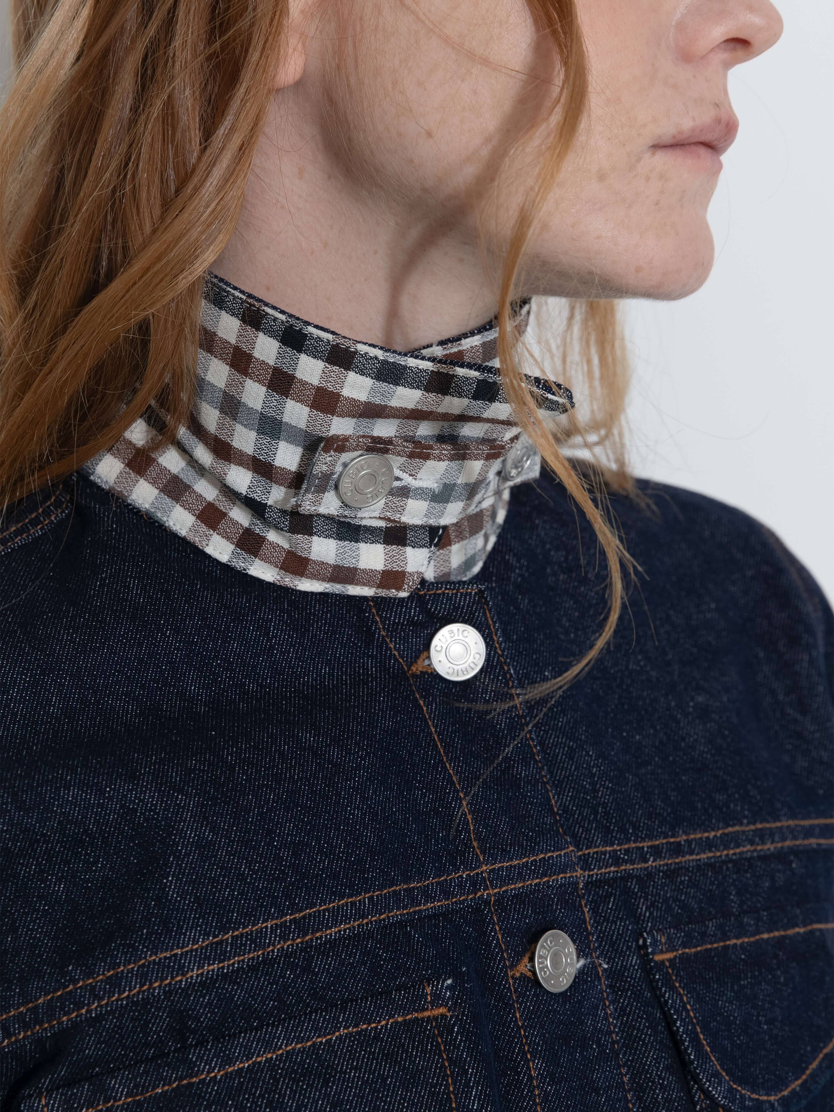 Person wearing a dark denim jacket with a plaid scarf around their neck.