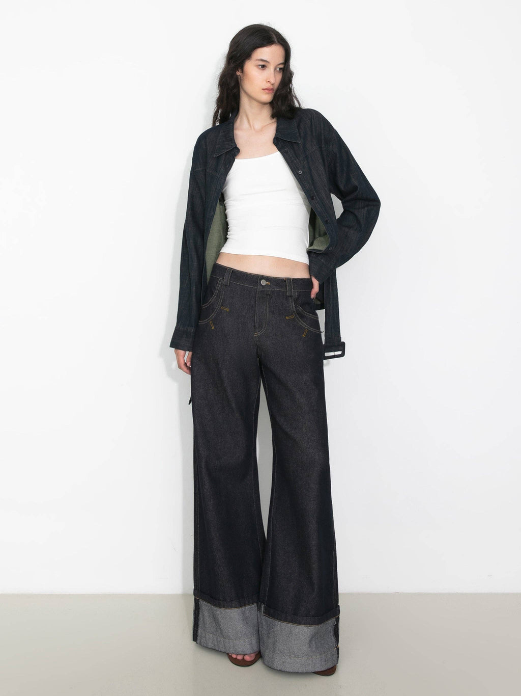 Woman wearing a black jacket, white top, and dark jeans on a white background