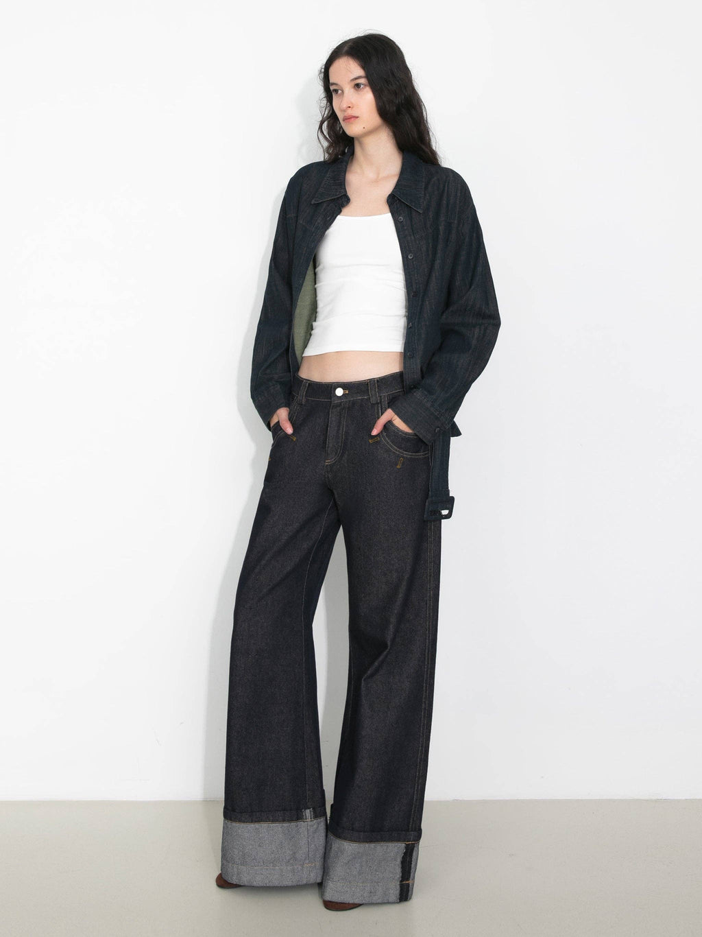 Woman wearing a white top and black wide-leg pants with a jacket on a plain background