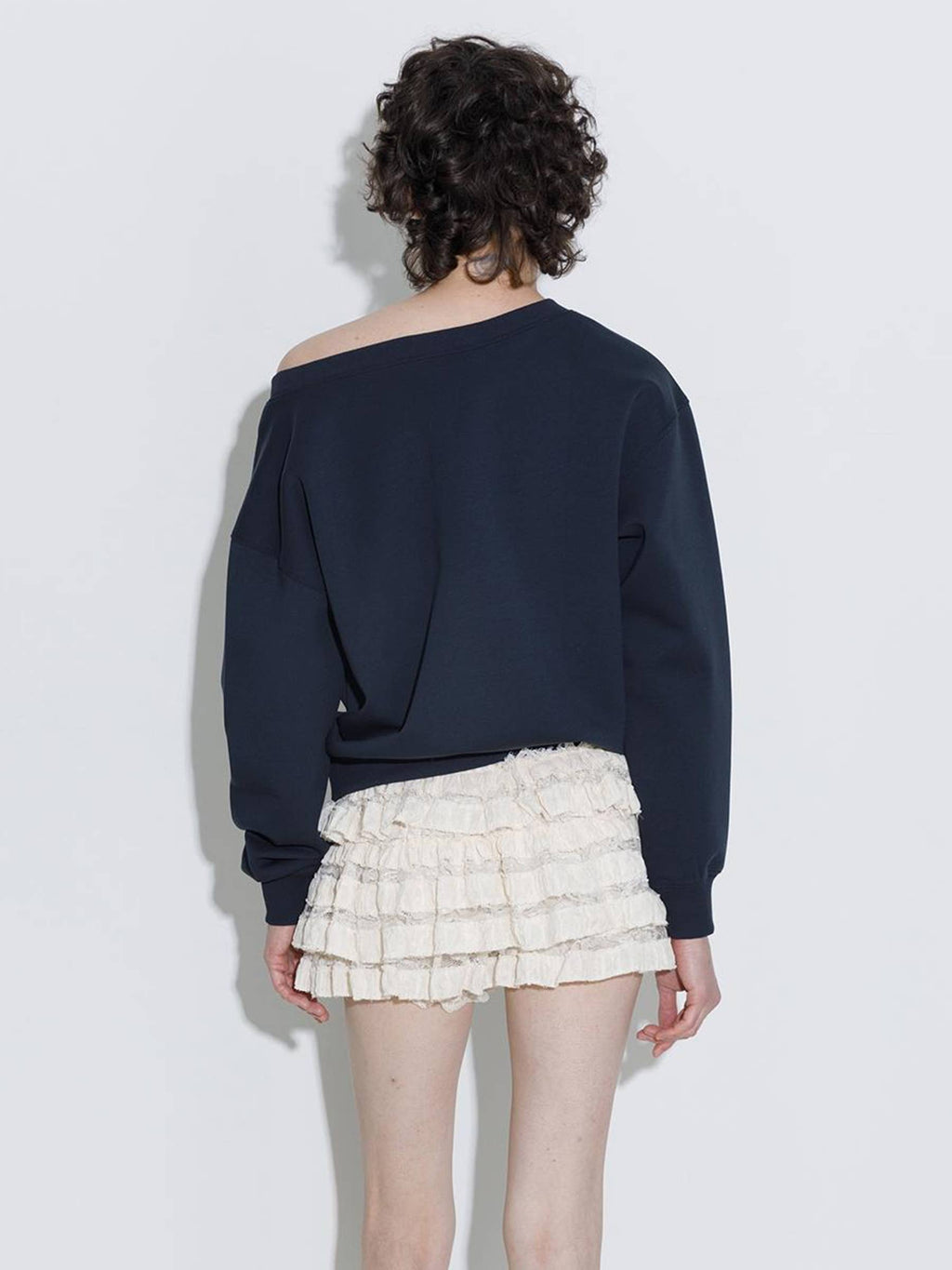 Person wearing a navy blue off-shoulder top and white ruffled skirt on a light gray background
