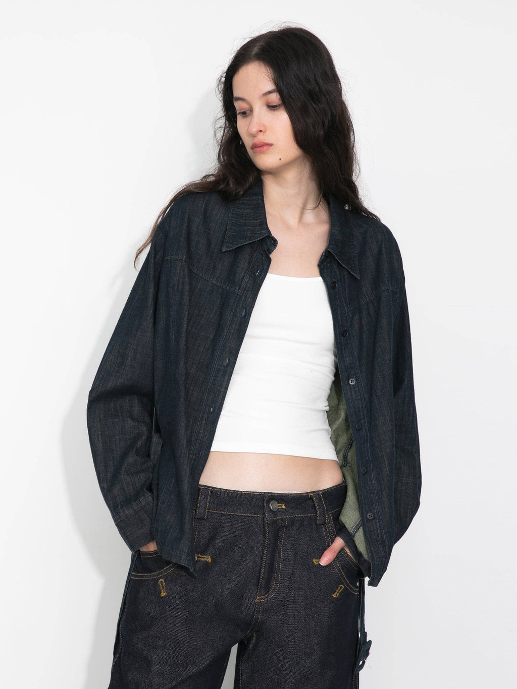 Woman wearing a dark denim jacket and pants with a white top on a plain background