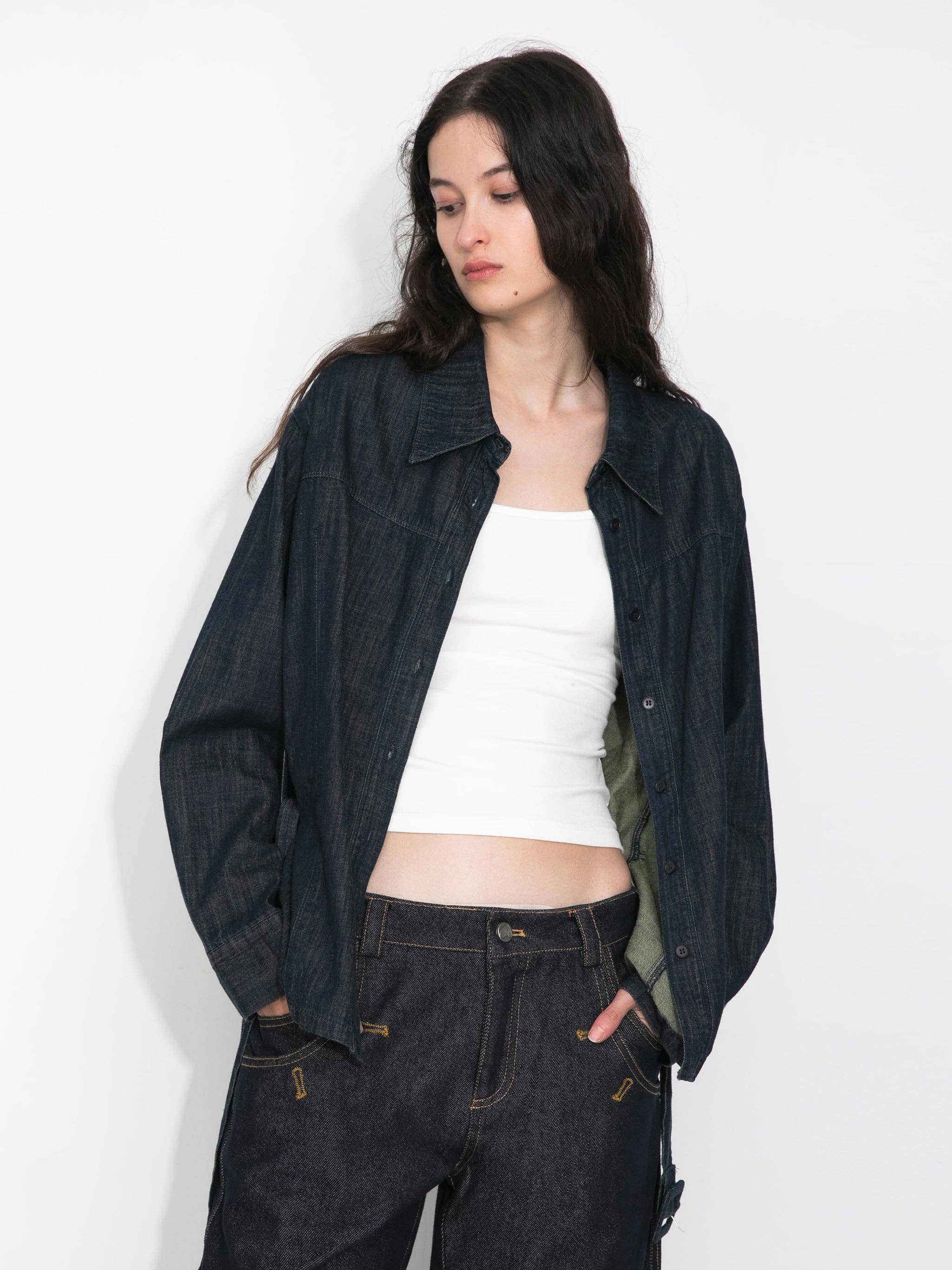 Woman wearing a dark denim jacket and pants with a white top on a plain background