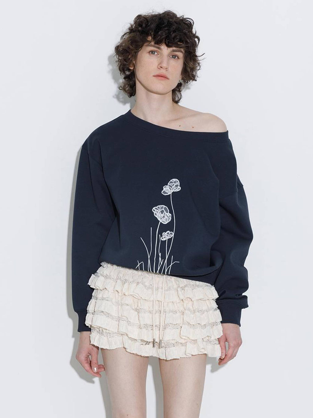 Person wearing a navy sweatshirt with floral design and a white ruffled skirt on a light background