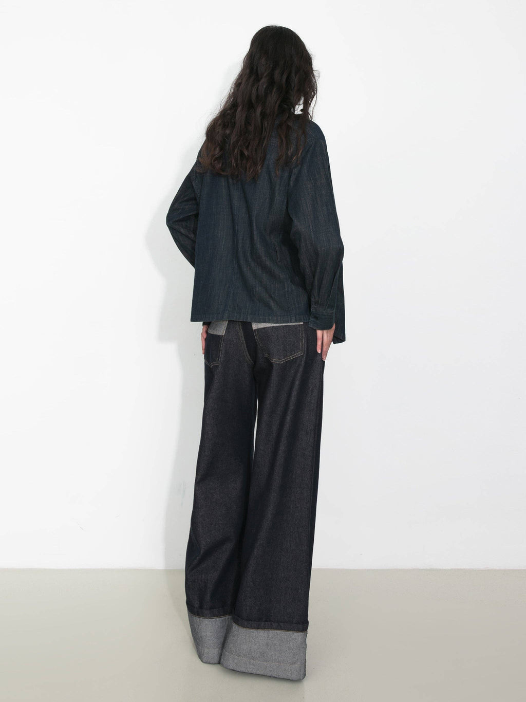 Person wearing a dark outfit with wide-leg pants against a white background