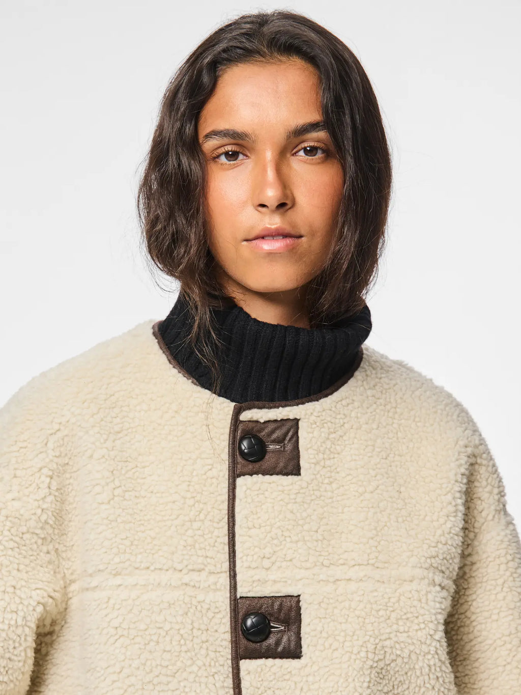 Person wearing a beige fleece jacket with black buttons on a white background