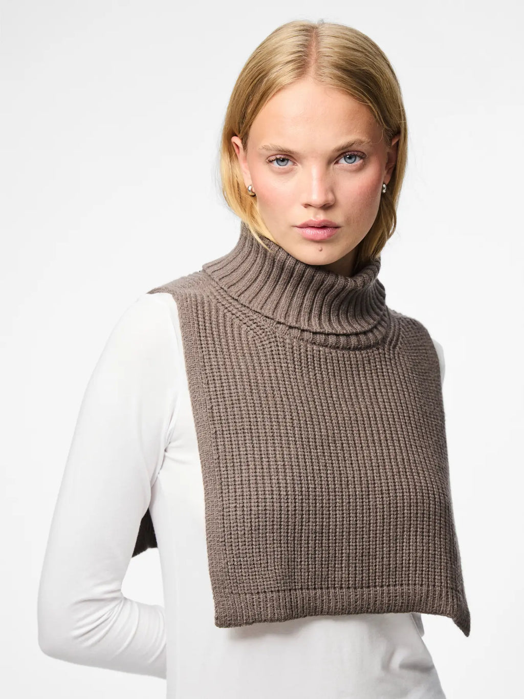 Woman wearing a brown knitted vest over a white long-sleeve shirt on a light gray background