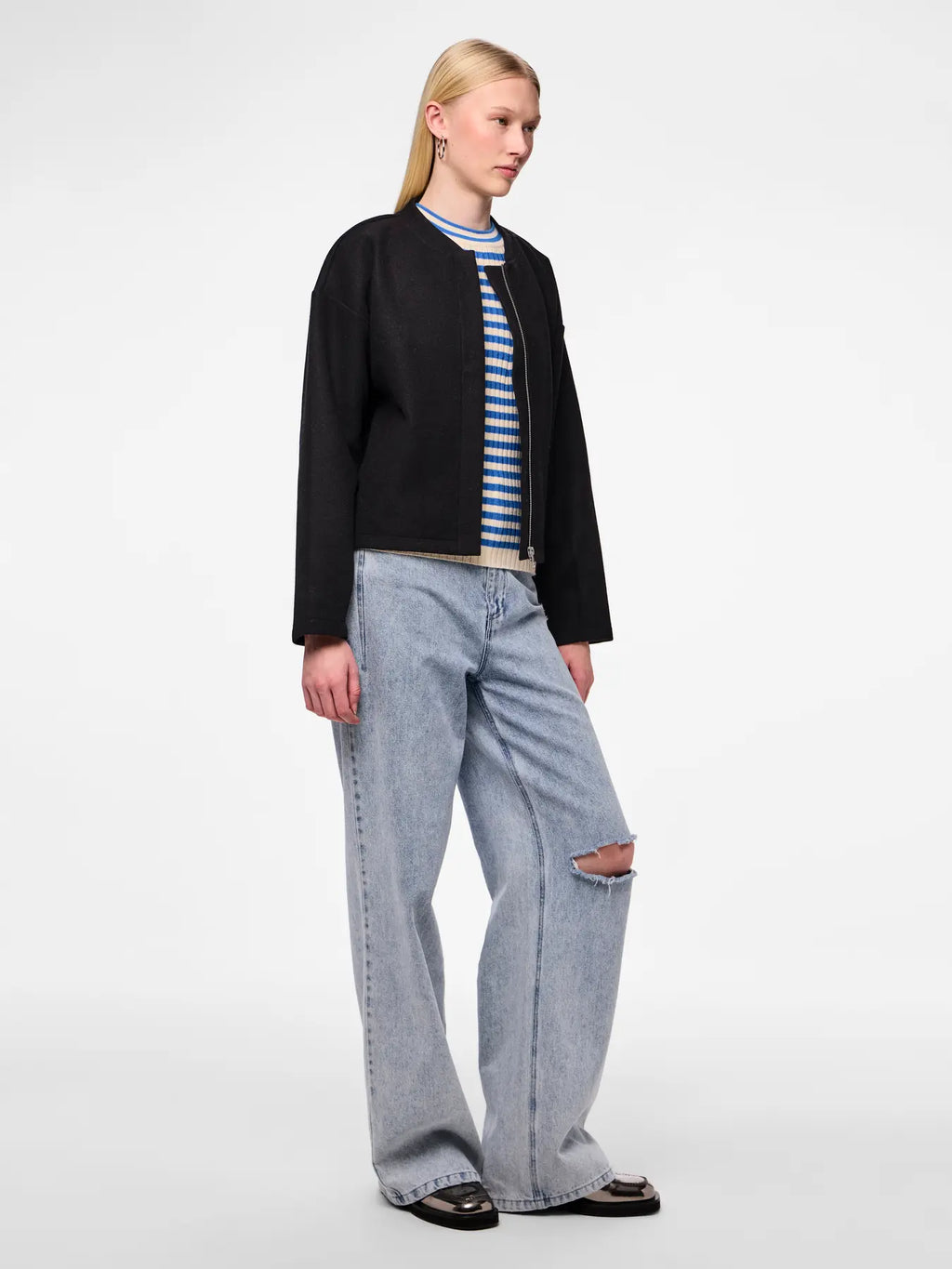 Person wearing a black jacket, striped shirt, and light blue jeans on a white background