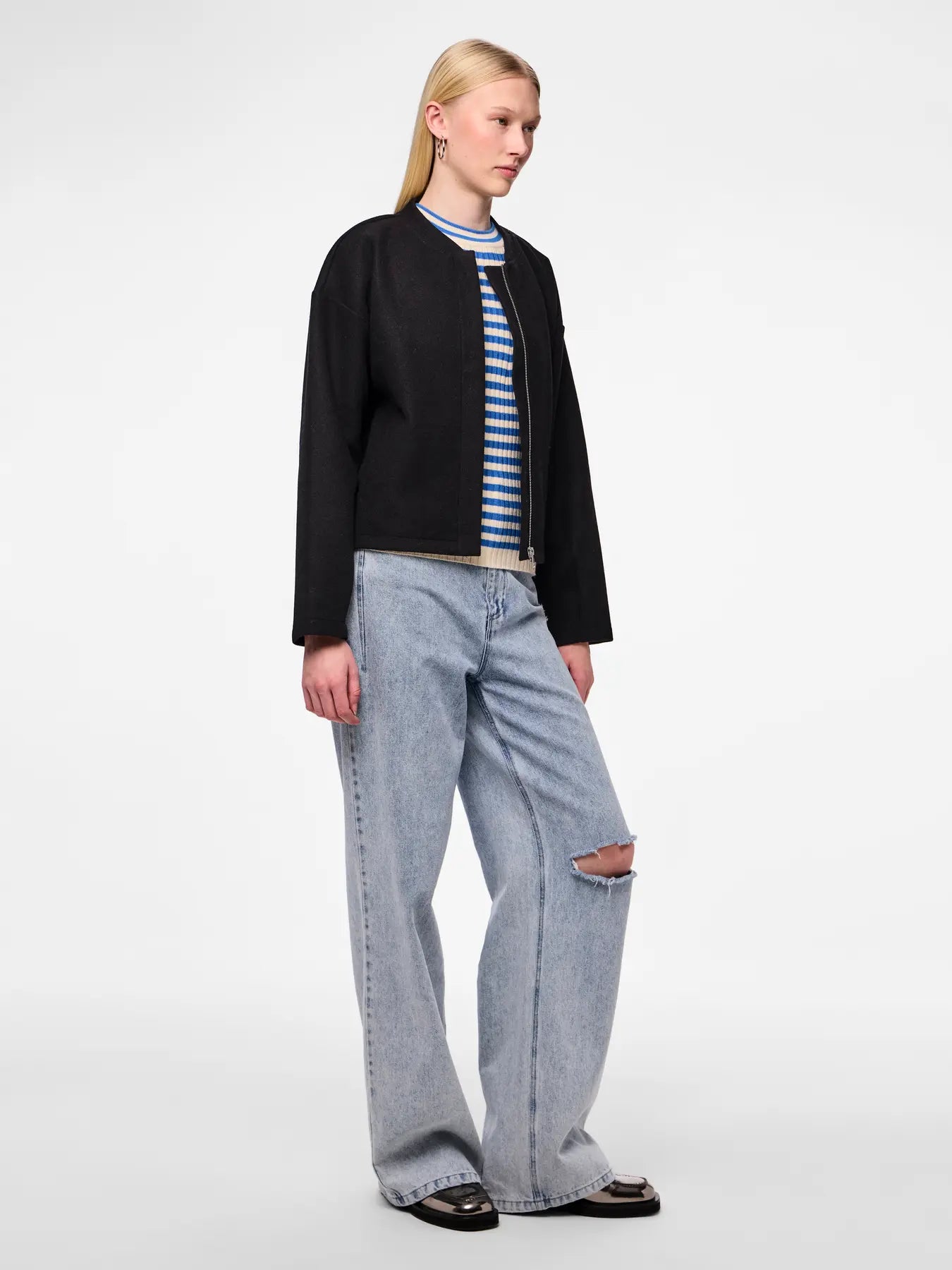 Person wearing a black jacket, striped shirt, and light blue jeans on a white background