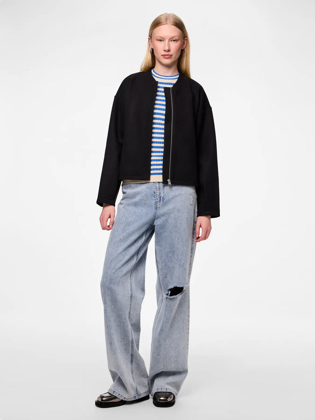 Person wearing a black jacket, striped shirt, and light blue jeans on a white background