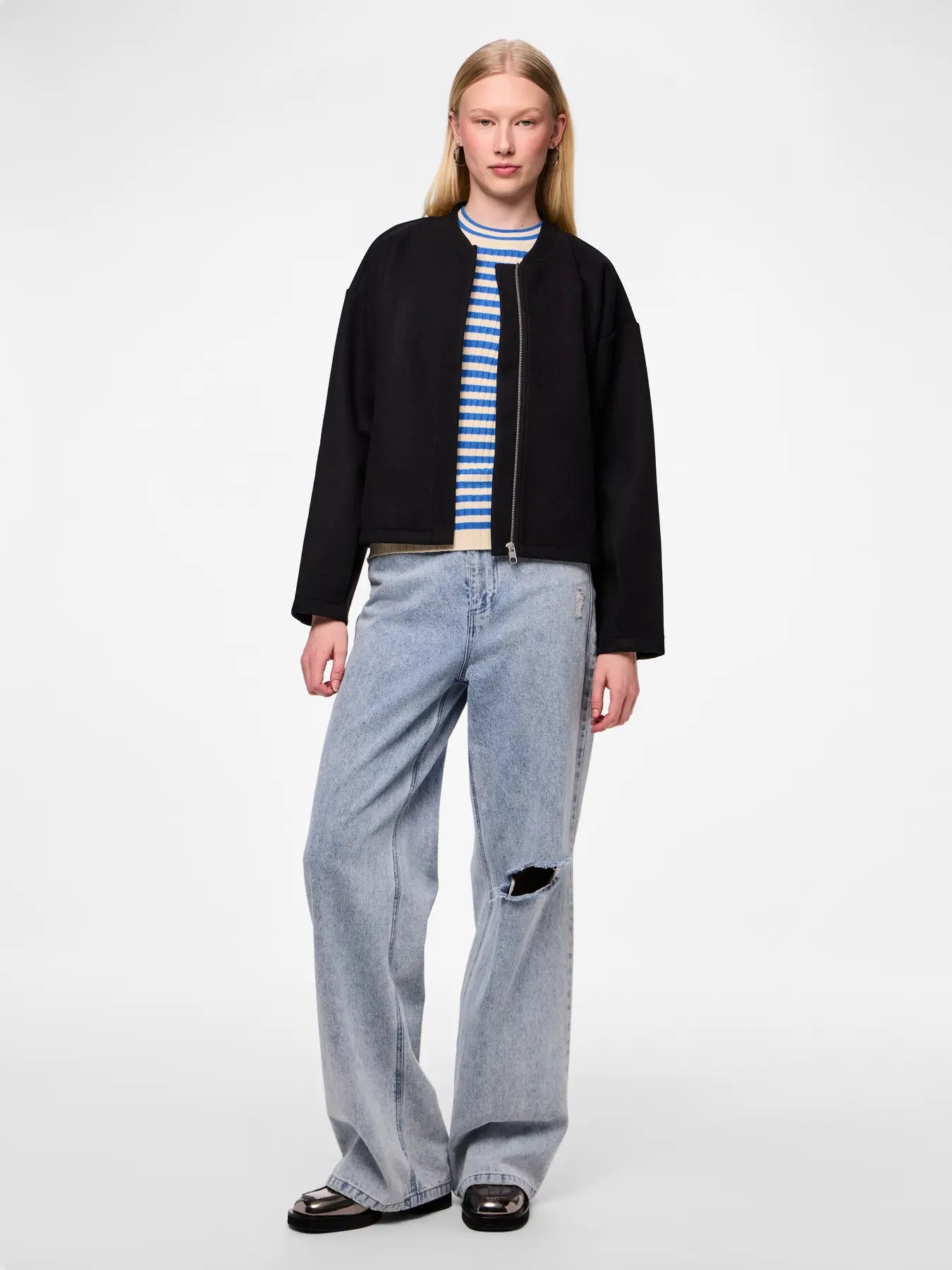 Person wearing a black jacket, striped shirt, and light blue jeans on a white background