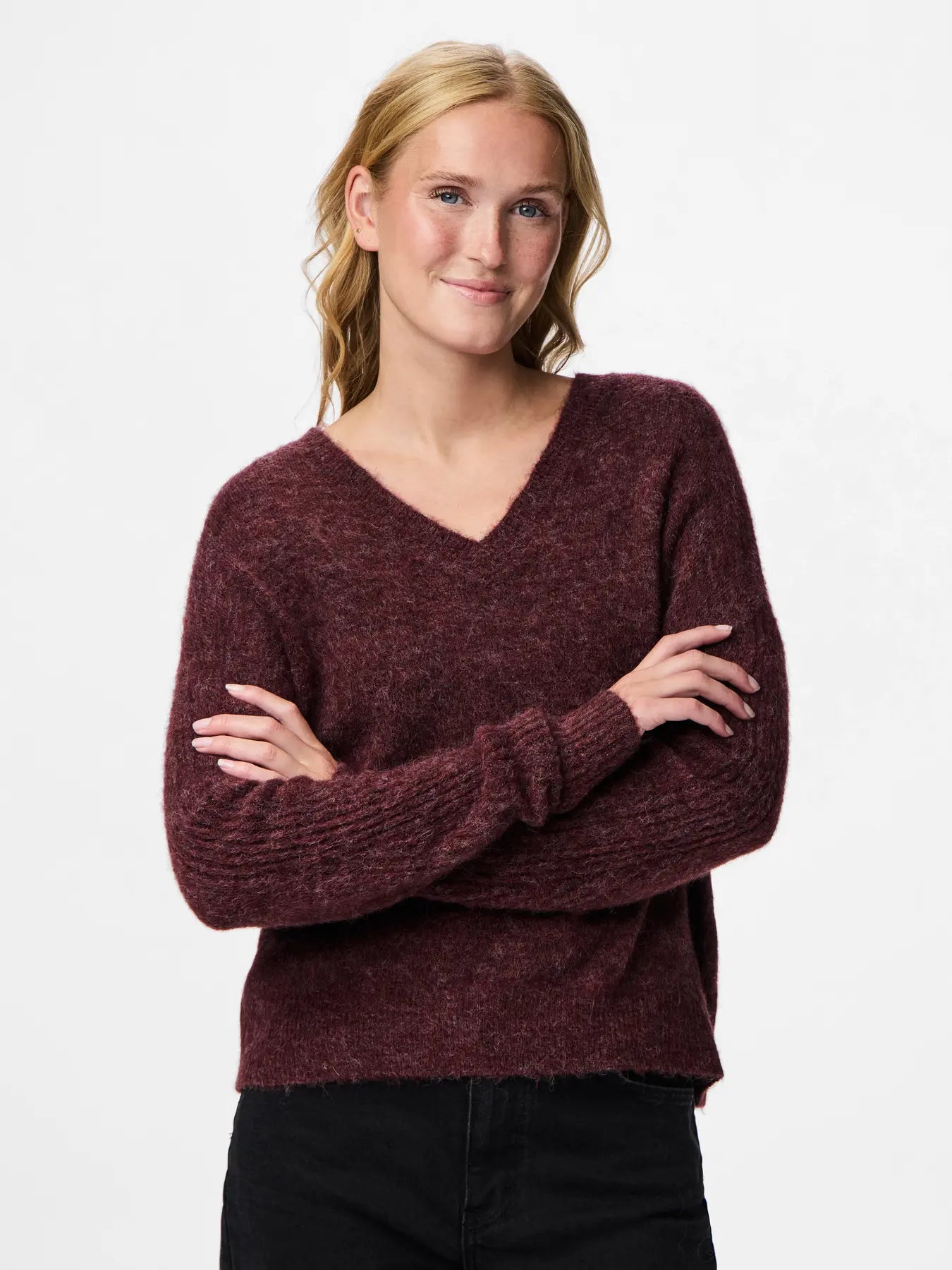 Woman wearing a maroon sweater with arms crossed on a white background
