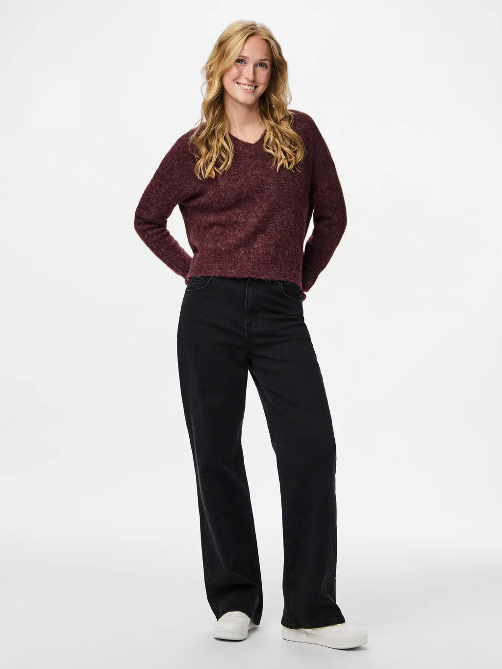 Woman wearing a maroon sweater and black pants on a white background