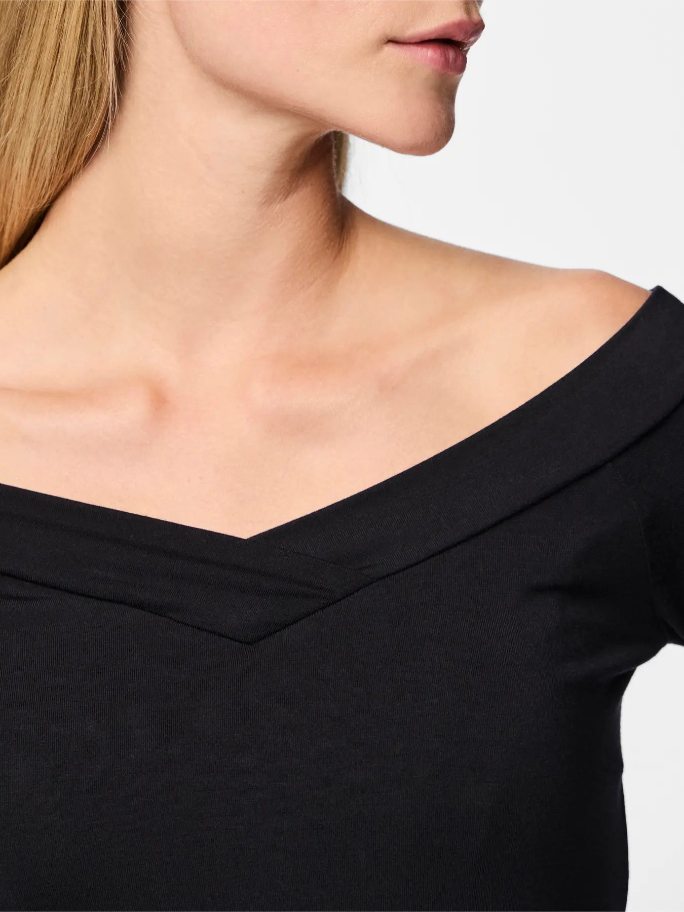 Black off-shoulder top worn by a person on a light gray background