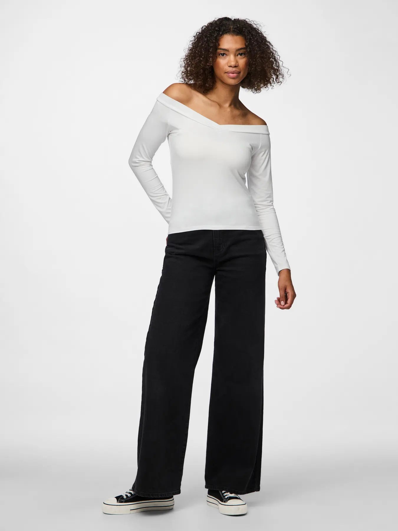 Woman wearing a white off-shoulder top and black pants on a white background