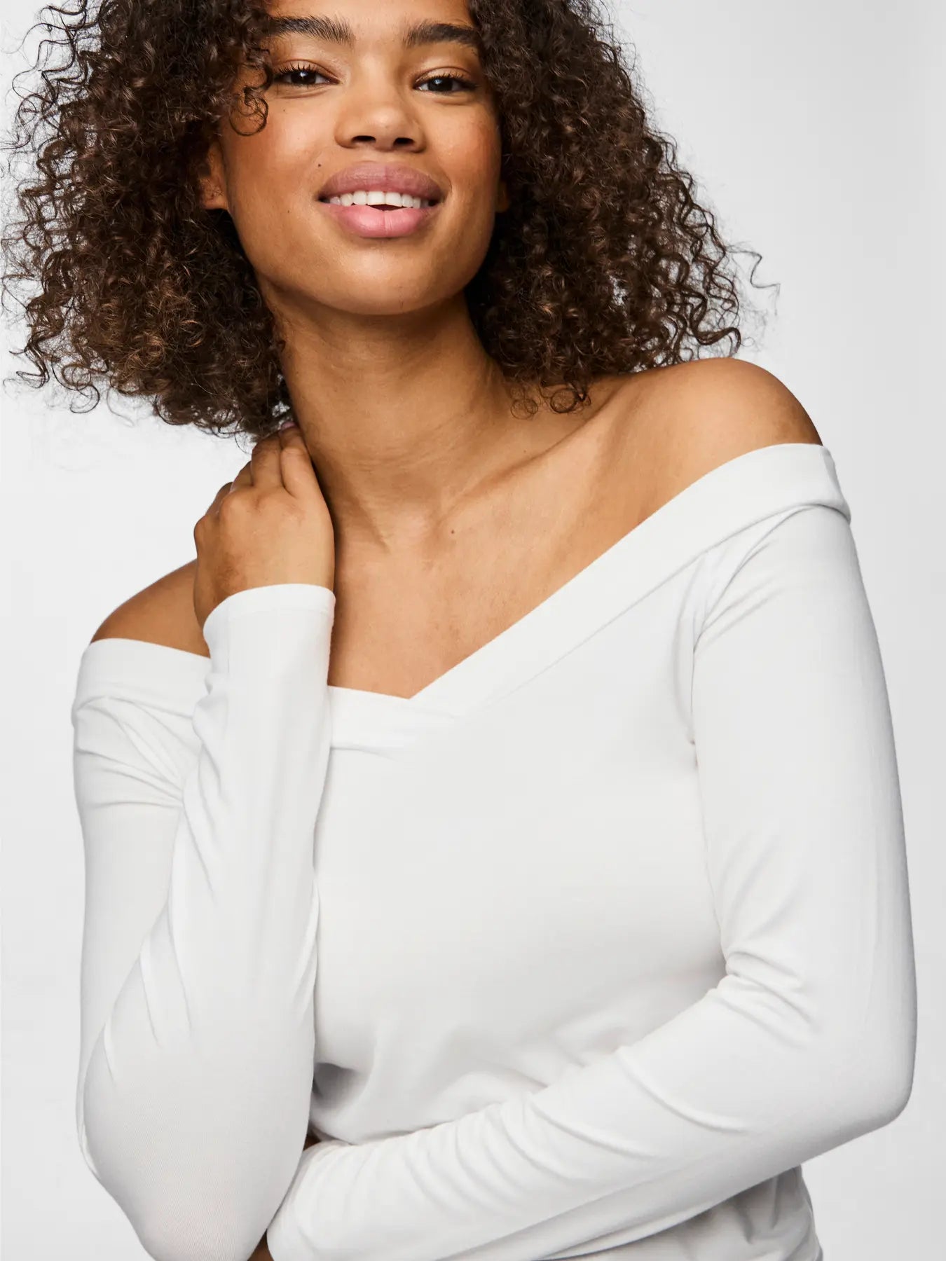 Woman wearing a white off-shoulder top against a plain background