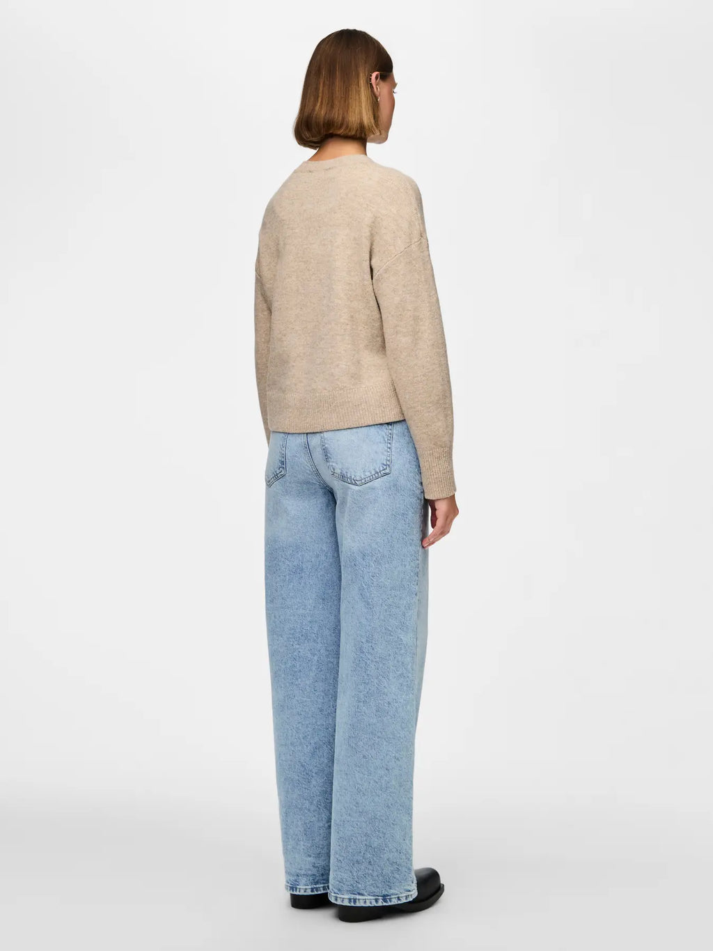 Person wearing a beige sweater and light blue jeans on a white background
