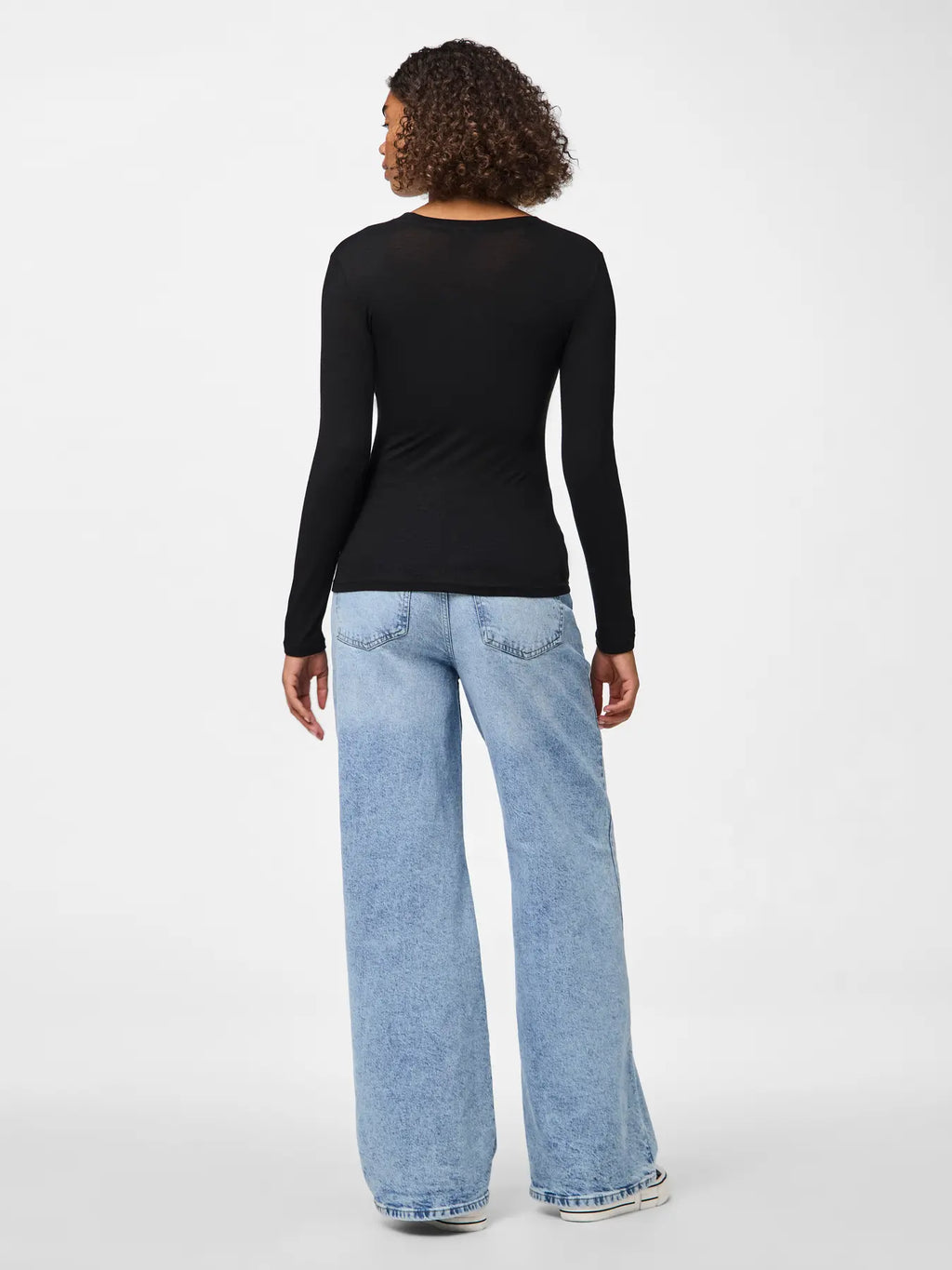 Person wearing a black long-sleeve top and light blue jeans on a white background