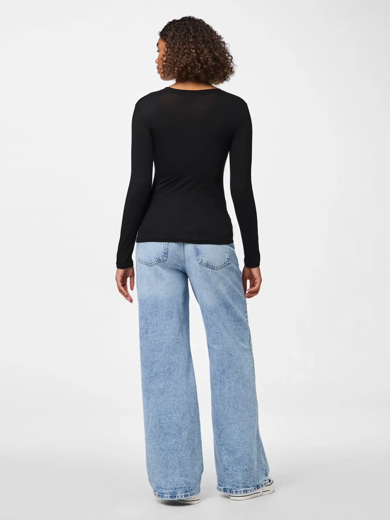 Person wearing a black long-sleeve top and light blue jeans on a white background