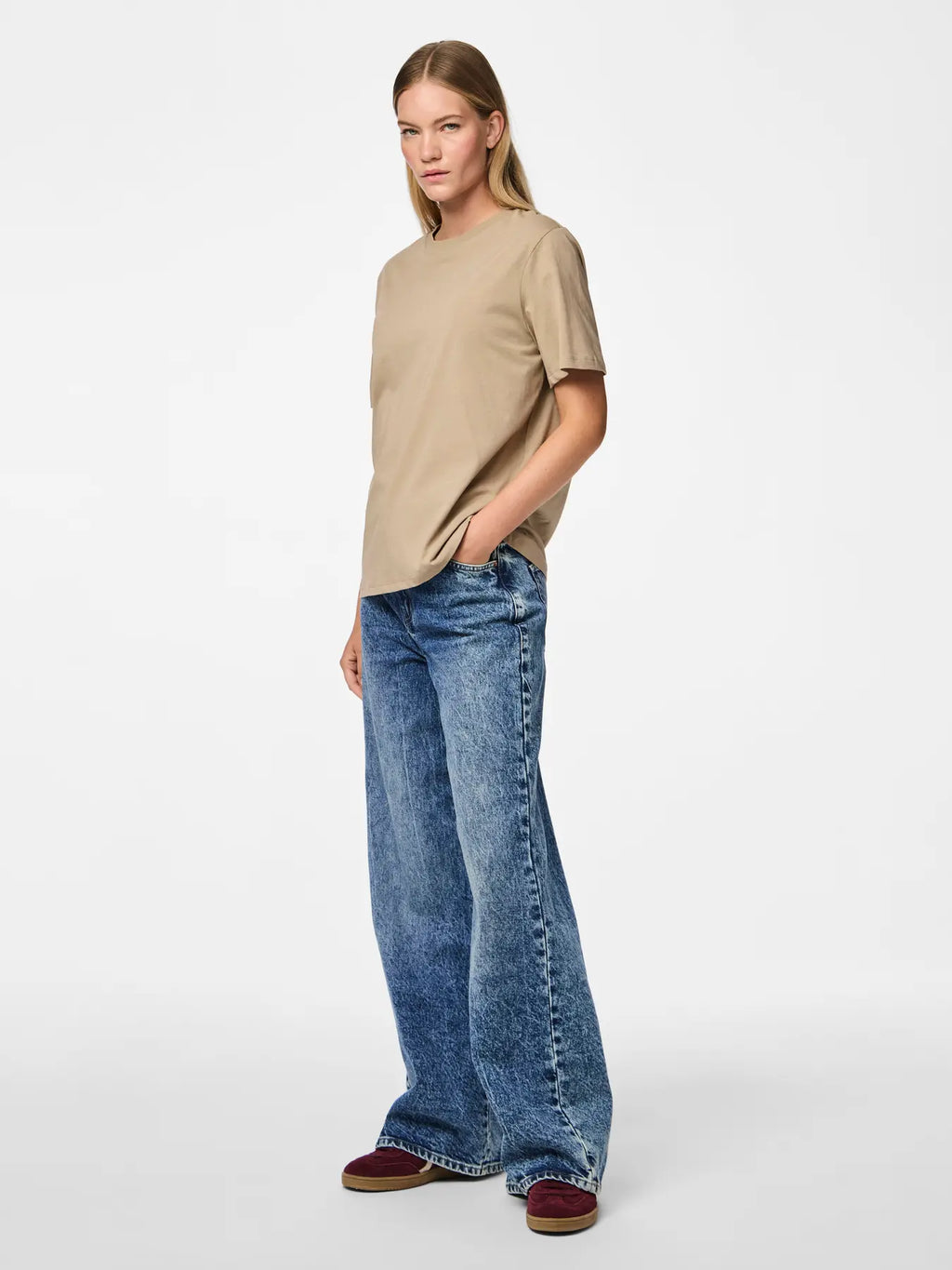 Woman wearing a beige t-shirt and blue jeans on a white background