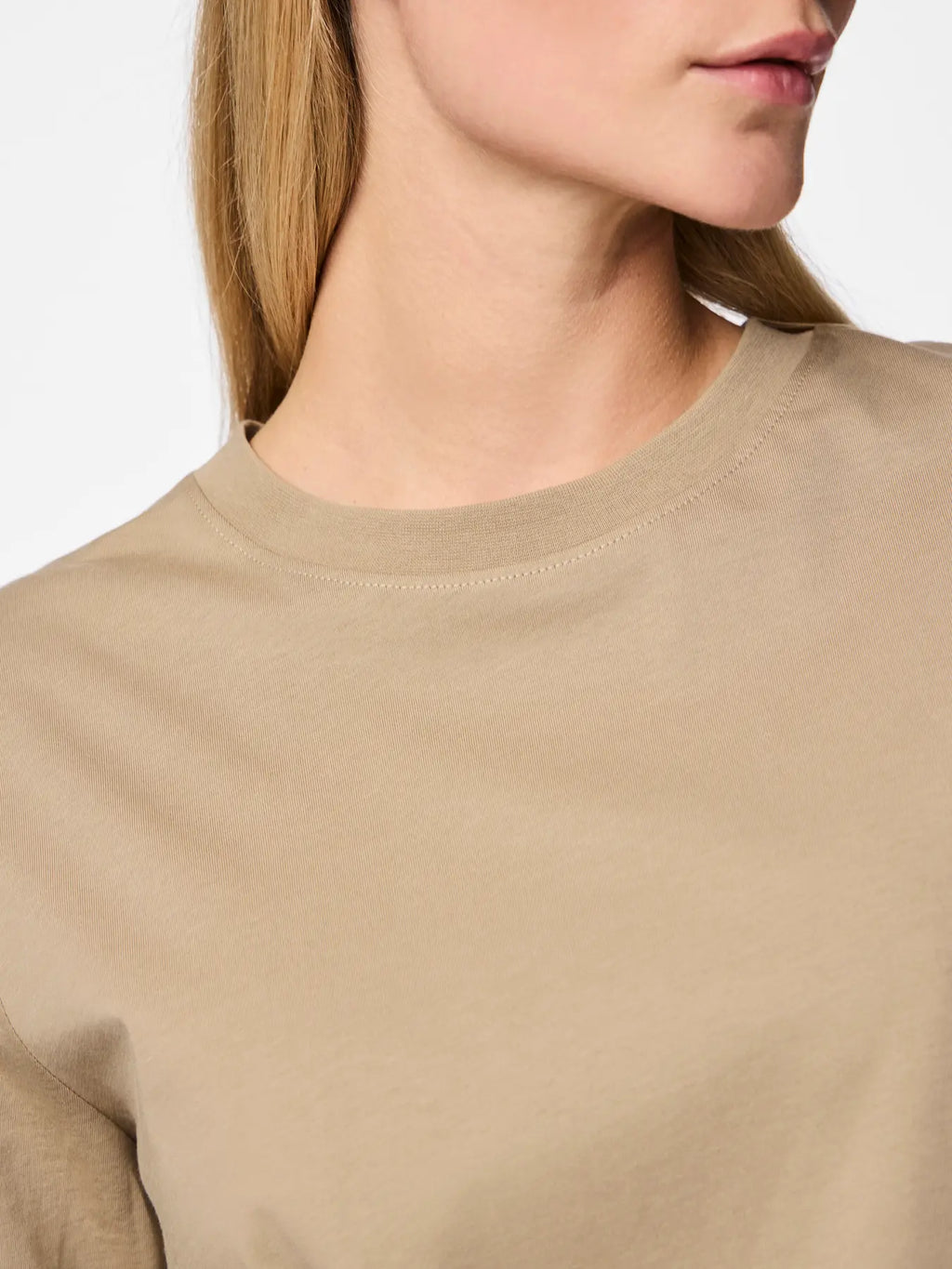 Close-up of a person wearing a beige sweater with a plain background