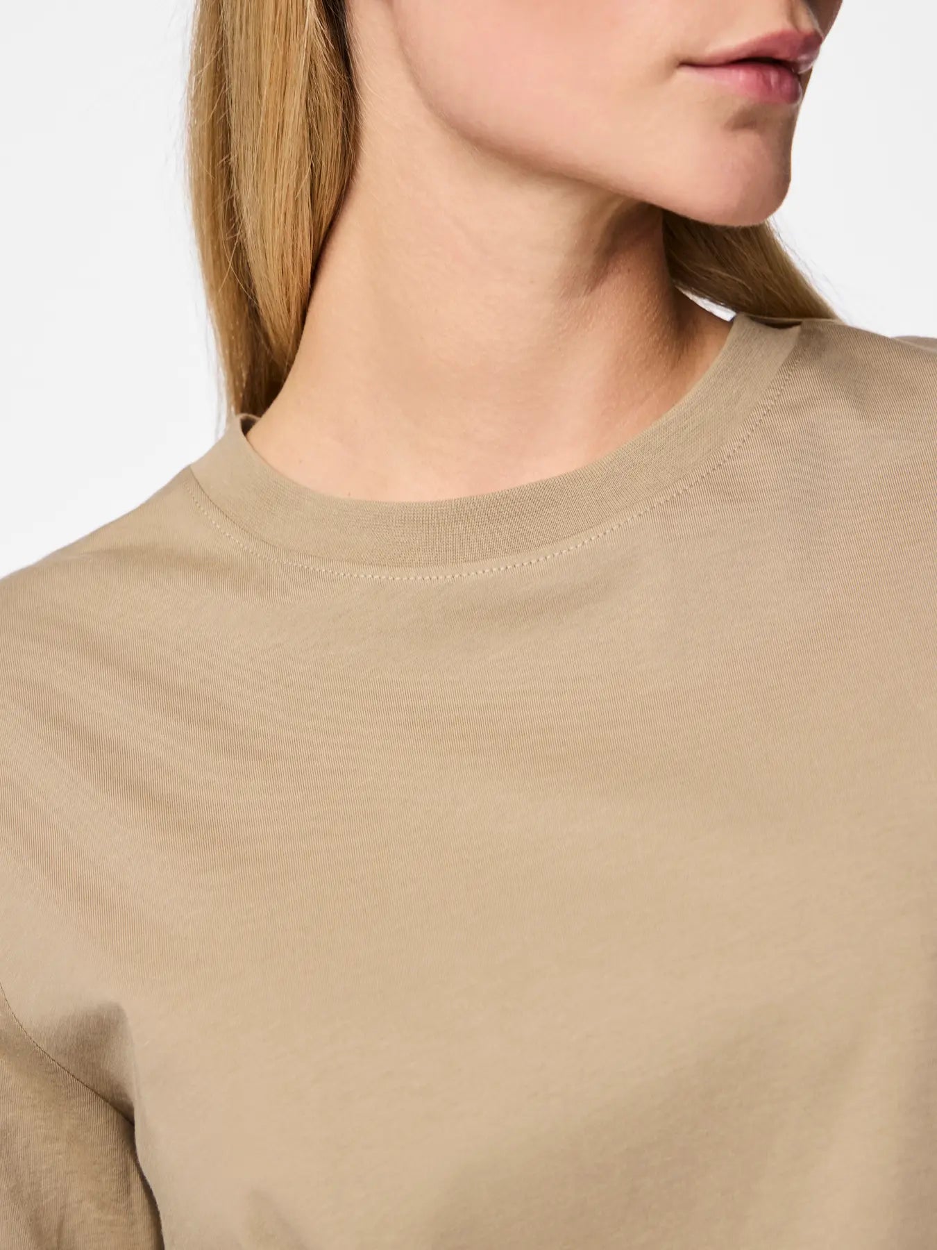 Close-up of a person wearing a beige sweater with a plain background
