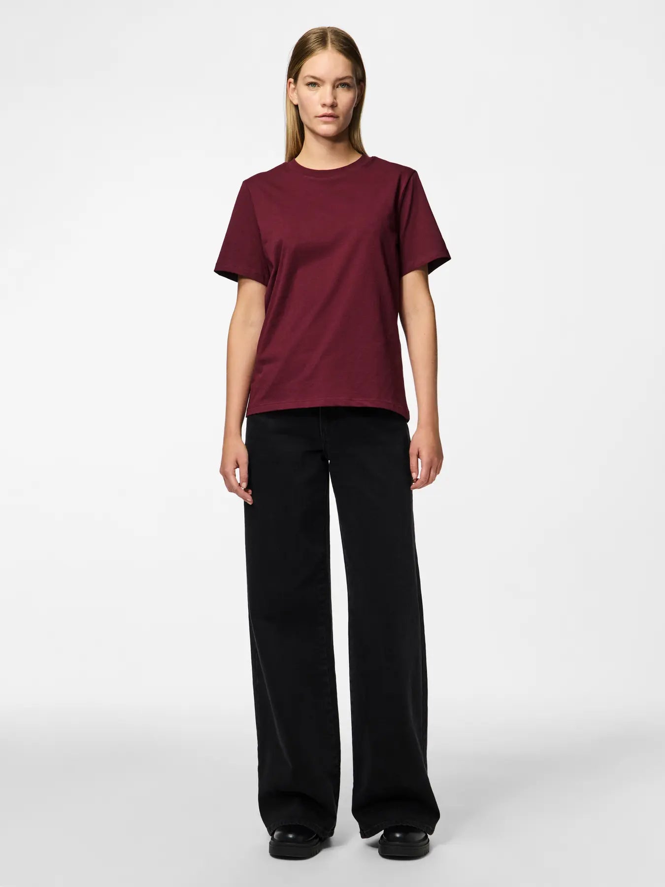 Person wearing a burgundy t-shirt and black pants on a white background