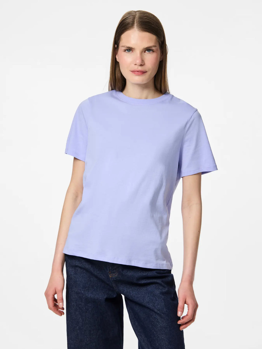 Woman wearing a light purple t-shirt and dark jeans on a white background