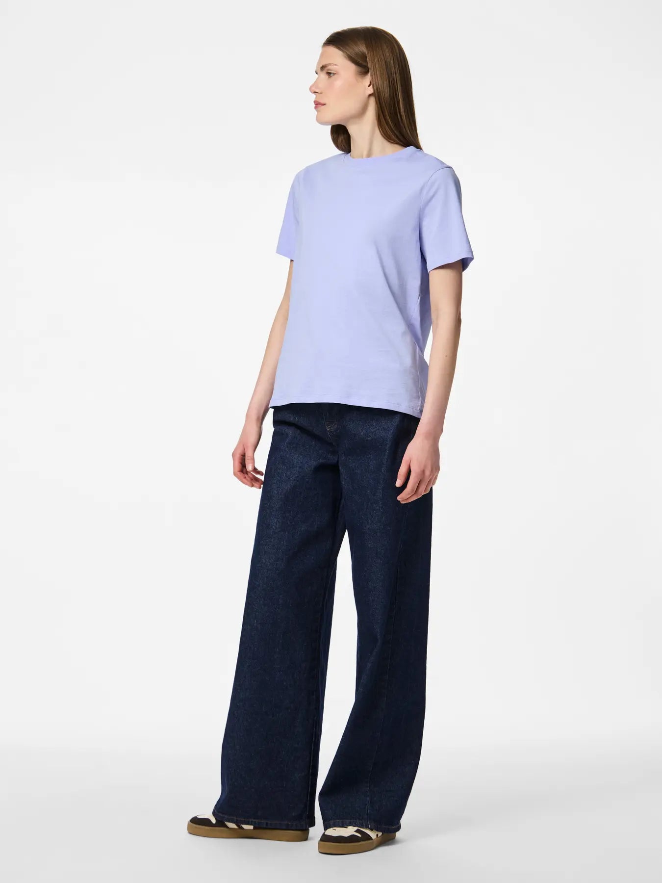 Woman wearing a light purple t-shirt and dark blue jeans on a white background