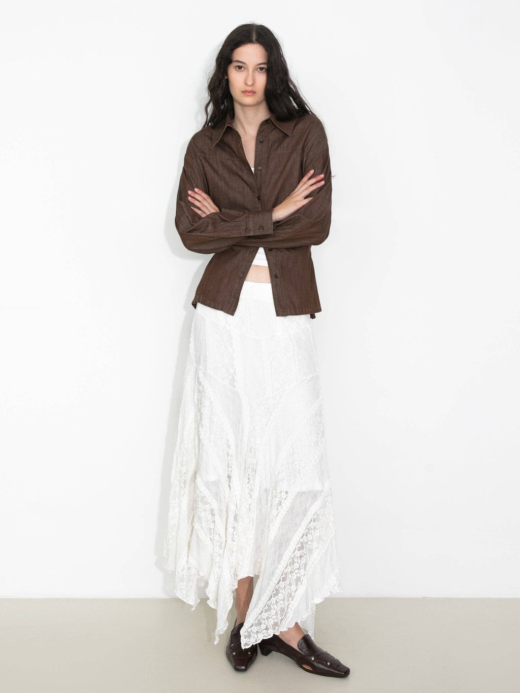 Woman wearing a brown shirt and white lace skirt on a plain background