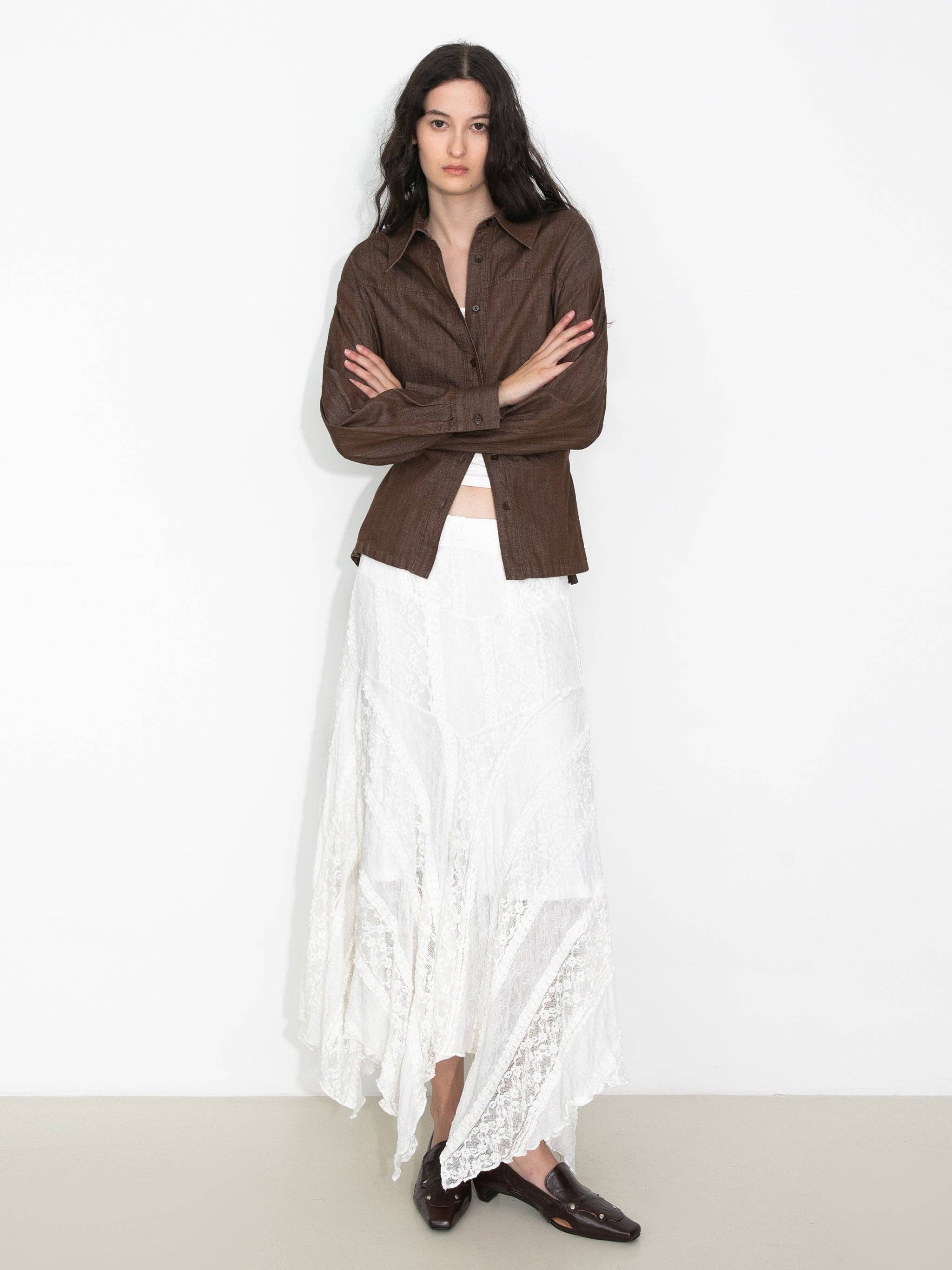 Woman wearing a brown shirt and white lace skirt on a plain background