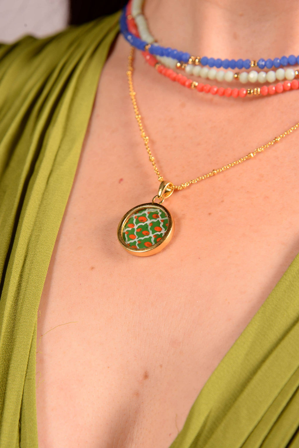 Close-up of a gold necklace with a green pendant worn by a person in a green top.