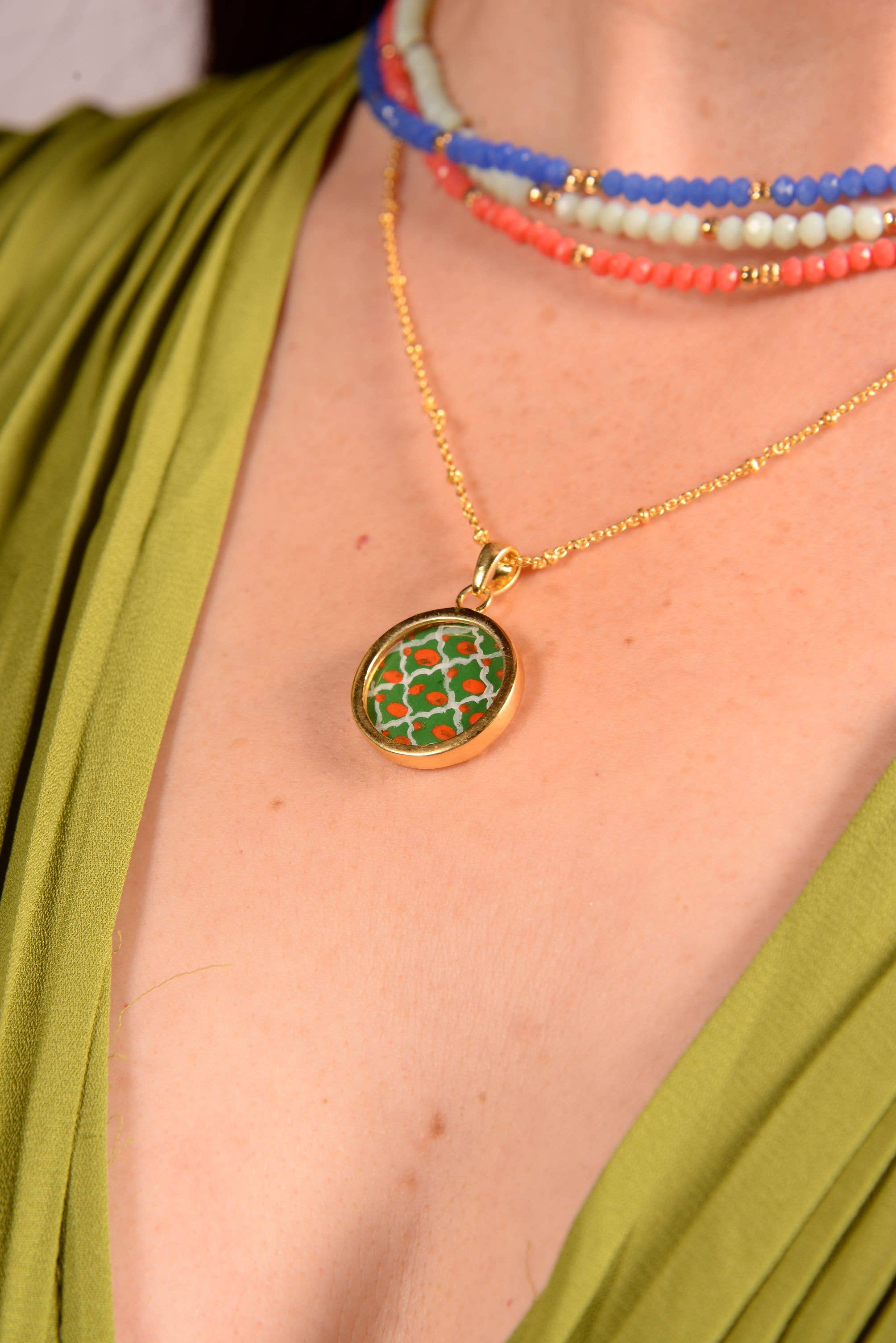 Close-up of a gold necklace with a green pendant worn by a person in a green top.