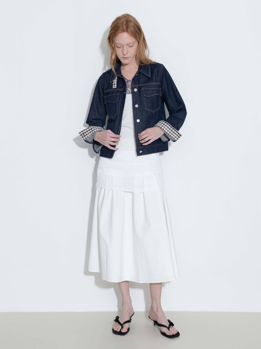 Woman wearing a denim jacket over a white dress on a plain background