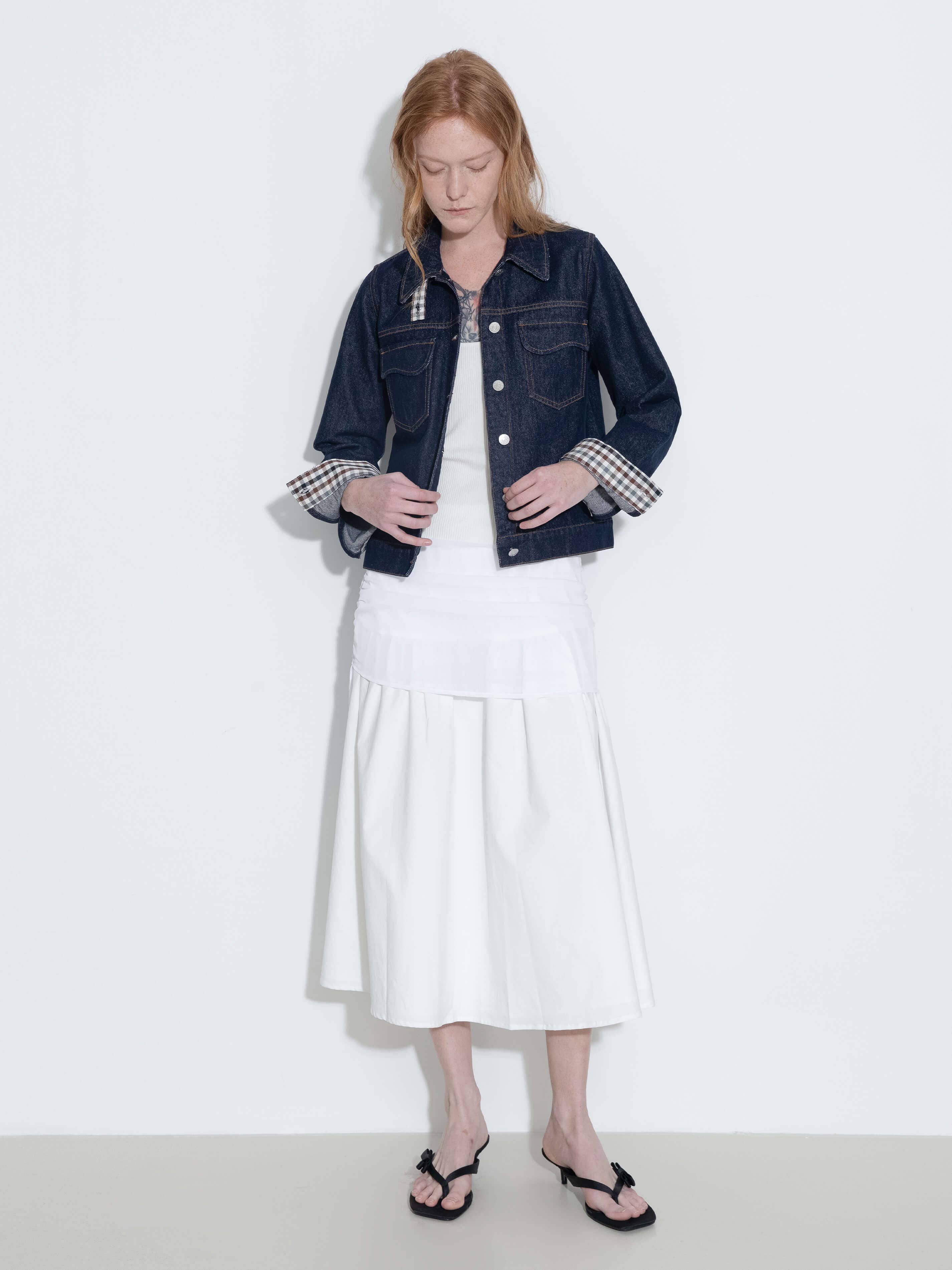 Woman wearing a denim jacket over a white dress on a plain background