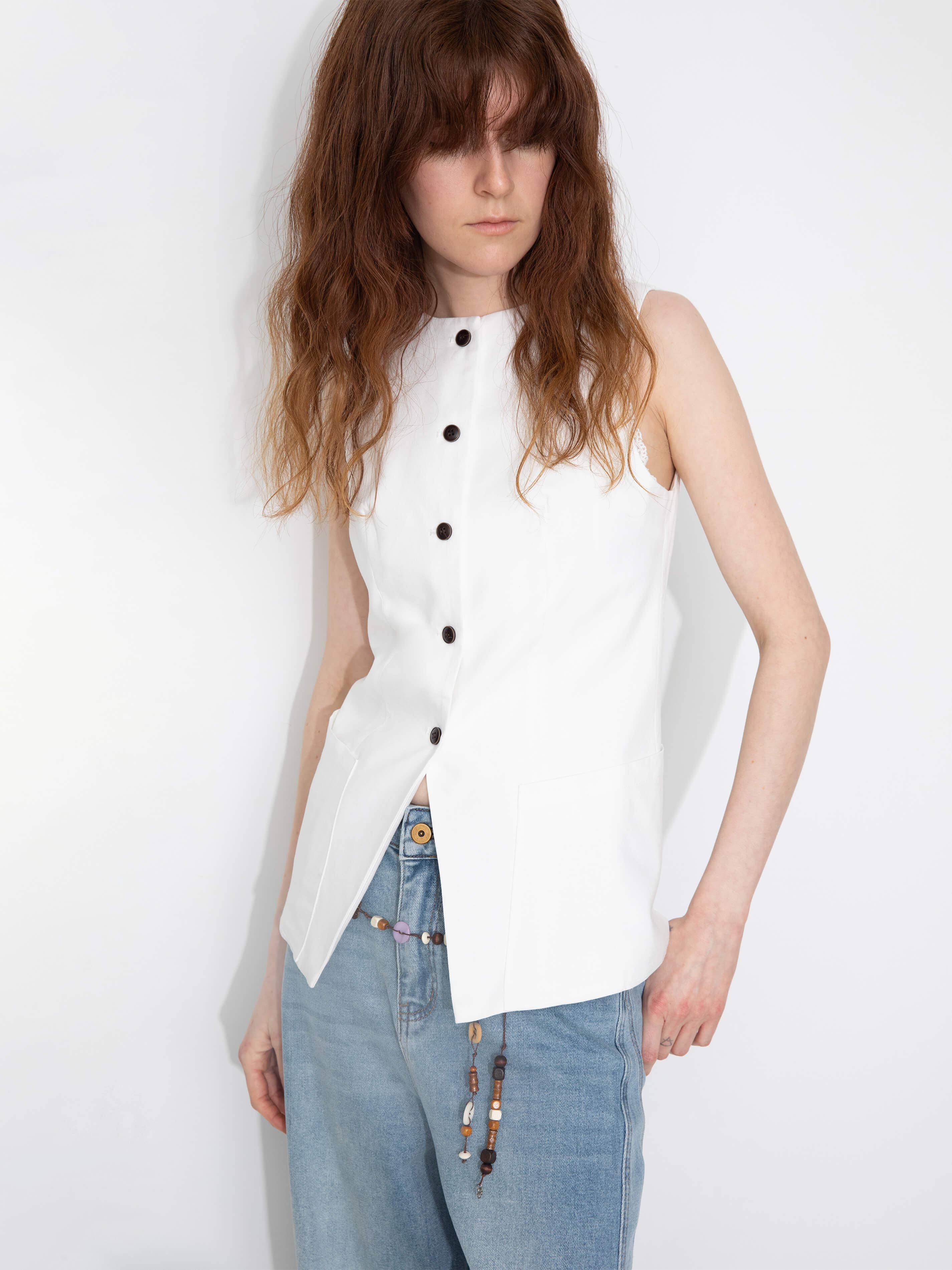 Woman wearing a white sleeveless button-up shirt and blue jeans on a white background
