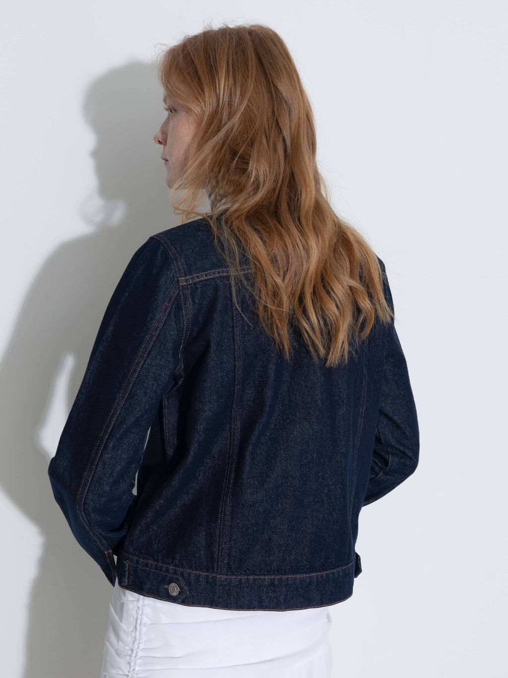 Person wearing a dark blue denim jacket against a white wall