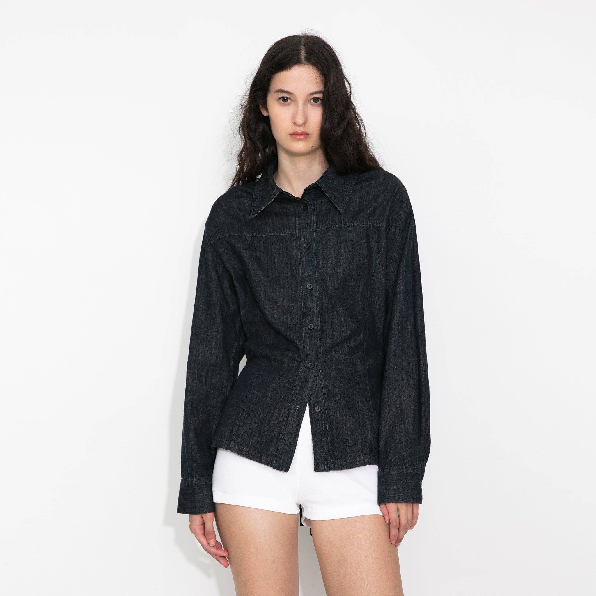 Woman wearing a dark denim jacket and white shorts on a plain background