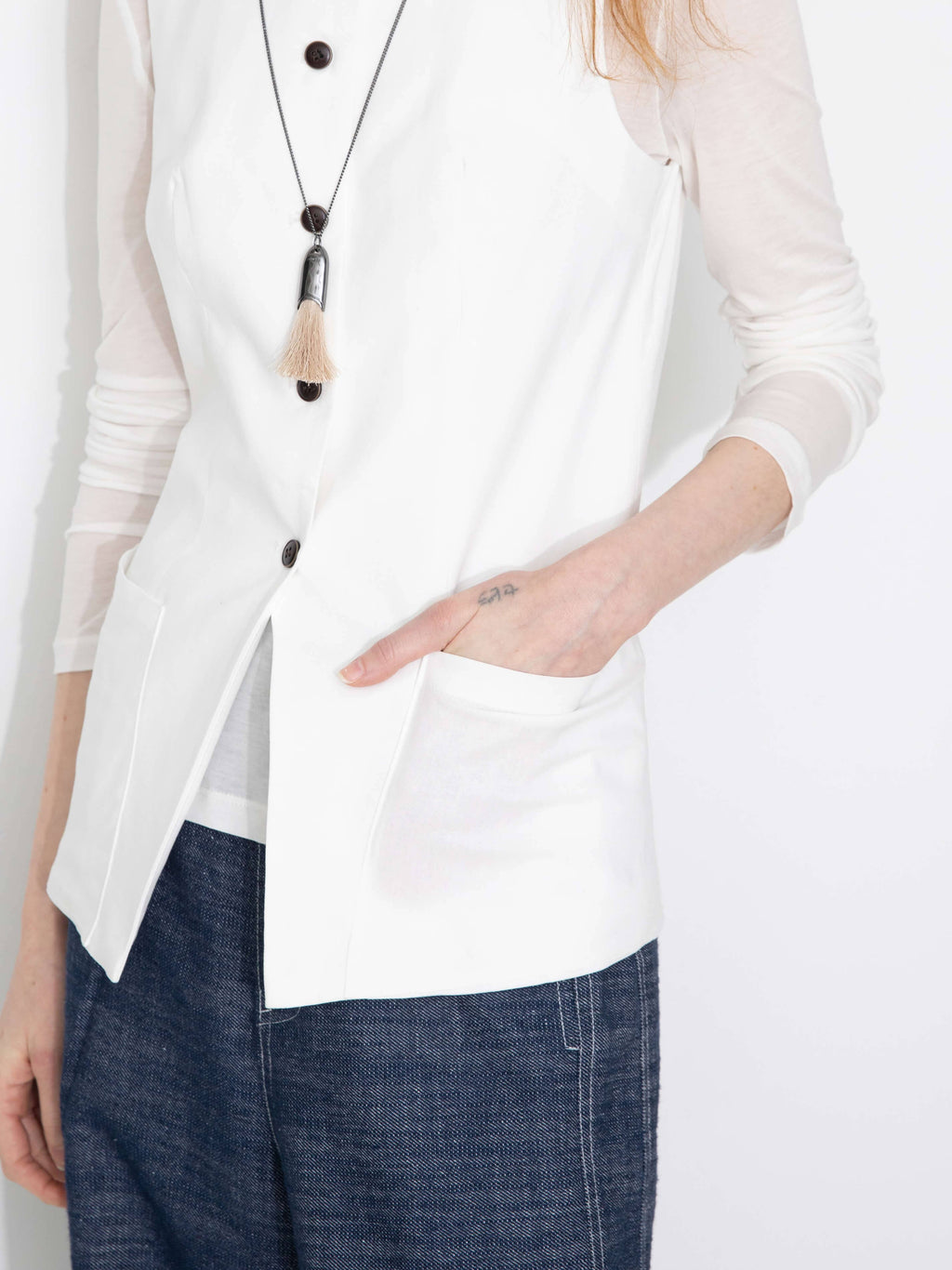 Person wearing a white blouse with a necklace and blue jeans on a plain background